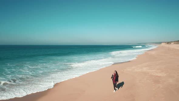 Young brunette woman walking along the Atlantic ocean coastline, enjoying a view of crashing waves