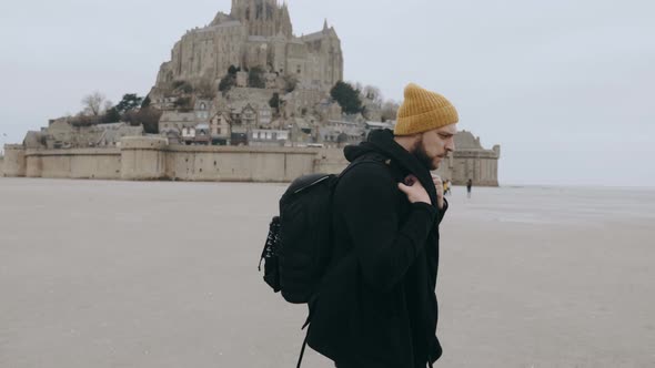 Happy Excited European Tourist Man with Backpack Walking Away From Epic Mont Saint Michel Castle in