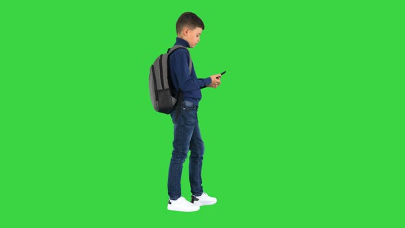 Schoolboy with a Backpack Using Mobile Phone on a Green Screen Chroma Key alt