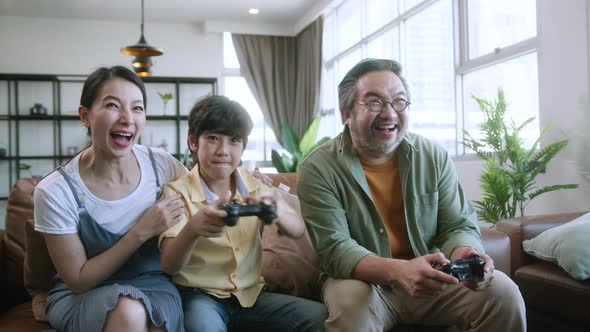 family quality time ,asian parent and son sit relax playing game console together laugh joyful