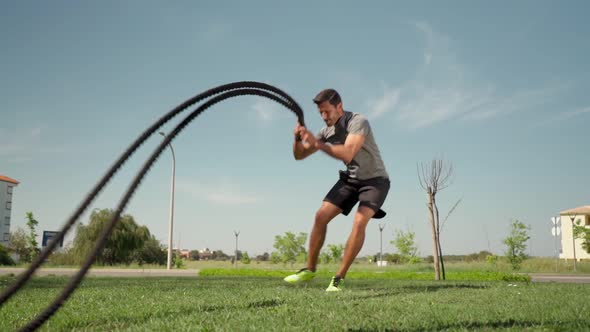 Muscular Caucasian Athlete Makes Waves with a Battle Rope on the Grass Outside
