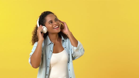 Happy young African American woman in casual wear listening to music on headphones and dancing