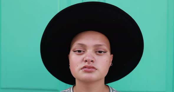 Trendy bald girl looking on camera while wearing a hat with colorful background alt