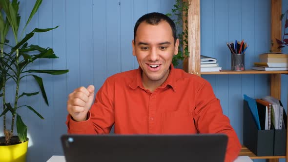 Young Business Man Gets Successful News Sits at Table with Laptop in Home Office
