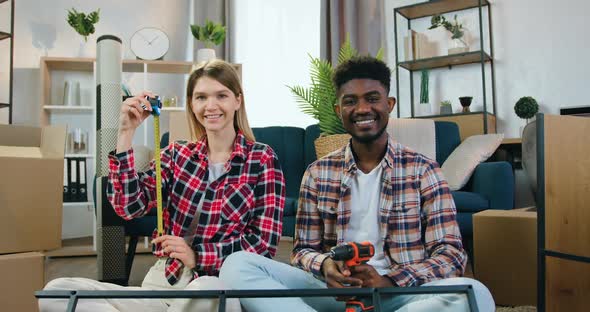Couple which Sitting on the Floor in New Bought Apartment and Posing on Camera with Tape Measure alt