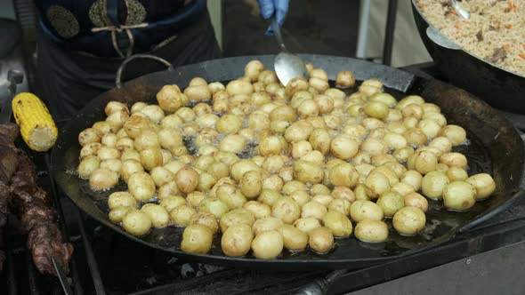 Peeled new potatoes are boiling in oil in a large frying pan. close-up of the cook 