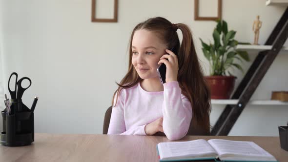 Caucasian Girl Sitting at Her Desk Talking on a Mobile Phone Using a Gadget and a Network alt
