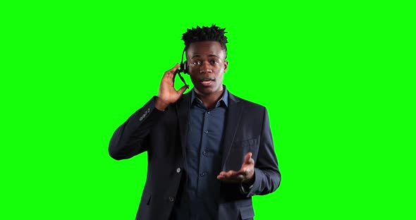 an African American man in suit using an earpiece and talking in a green background