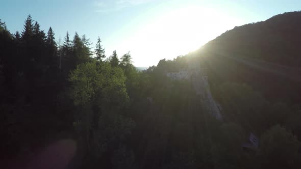 Aerial of sun shining behind forest and Bran Castle
