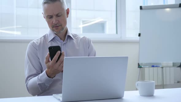 Middle Aged Businessman Busy Using Smartphone for Work in Office alt