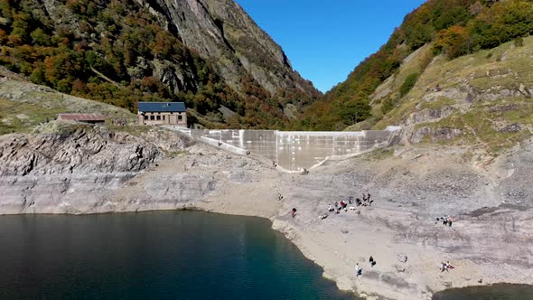 Lac d'Oô artificial lake in the French Pyrenees with visitors scaling the dam rock wall ridge, Aeria alt