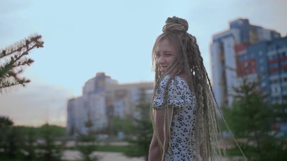 A Cute Young and Happy Girl with Dreadlocks Walks Down the Street and Poses