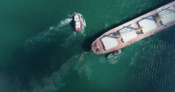  Large cargo ship enters the port escorted by tugboats alt