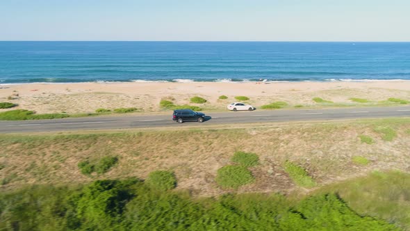 Drone Chasing Fast Driving Black SUV Along Coastal Asphalt Road with Crashing Waves in the alt