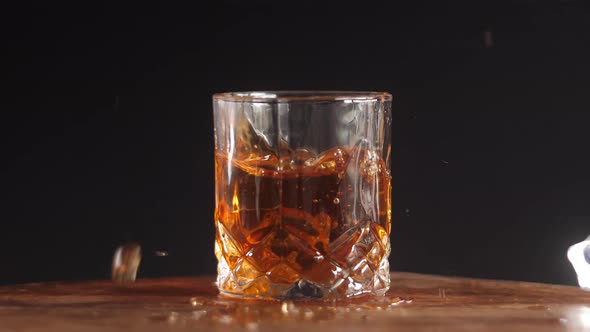 Whiskey glass with ice cube splash in slow motion