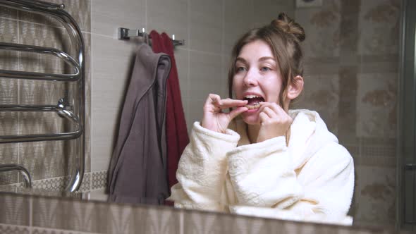 Front View Through a Mirror of a Woman in the Bathroom Removing an Invisible Clear Aligner From Her alt