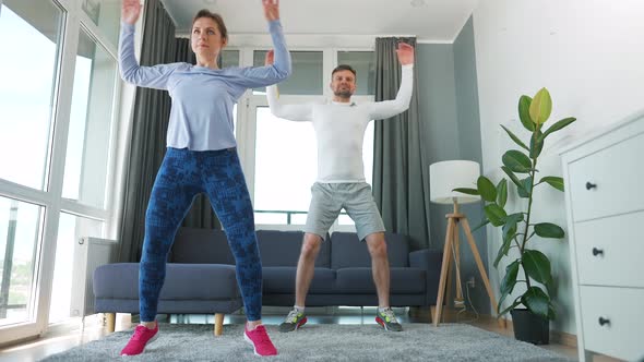 Caucasian Couple is Doing Jumping Jacks Exercise at Home in Cozy Bright Room Slow Motion alt