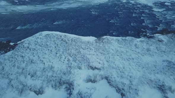 Aerial View Flying Over Mountain Cliff To Reveal Rushing Water Below Winter Iceland
