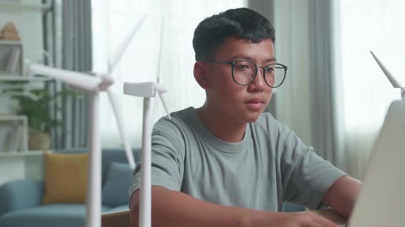 Asian Kid Or Student With Laptop Computer Programming Electric Wind Turbine Model At Home alt
