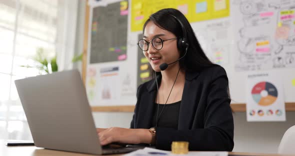 Happy female glasses wears headset video calling on laptop alt