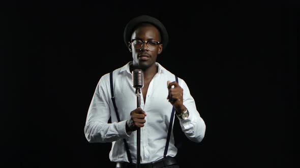 African American in a Studio Is Singing Songs Into a Microphone. Black Background alt