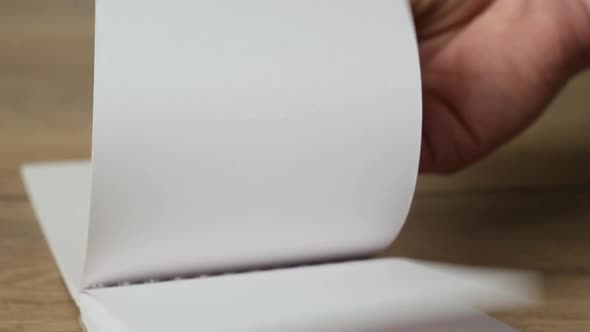 Hand flipping empty notebook pages on a wooden table. Close up. HD alt