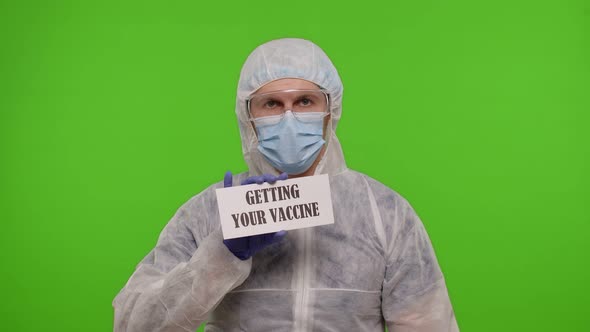 Medical Worker Doctor in PPE Suit with Syringe Ampoule Text Slogan on Paper Getting Your Vaccine alt