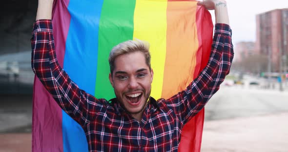 Gay man with makeup on having fun holding lgbt rainbow flag outdoor alt