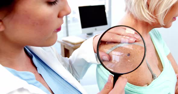 Dermatologist examining mole with magnifying glass alt