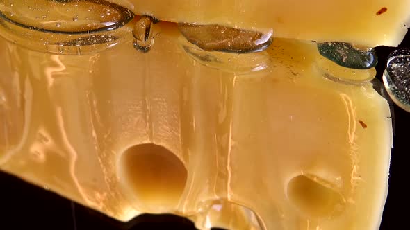 Drops of honey flow down from the cheese on a mirrored black background. alt