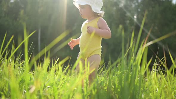 Little Funny Cute Blonde Girl Child Toddler in Yellow Bodysuit and White Hat Walking in Field with