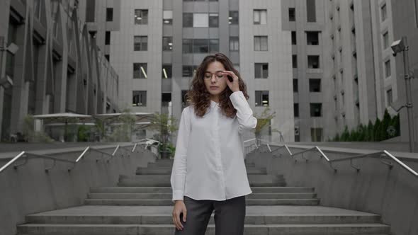 Young Girl Dressed In Business Style Clothes Stands On The Background Of Tall Building alt