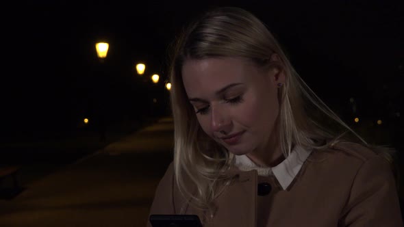 A Young Beautiful Woman Takes Selfies with a Smartphone in an Urban Area at Night alt