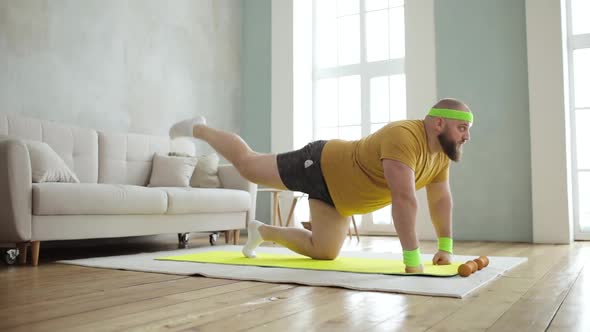 Fat Man in Sportswear Doing Legs Lifting Exercises on Mat on Knees at Home