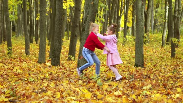 Two beautiful little girls play in the autumn Park, rejoice, laugh and hug . there are a lot