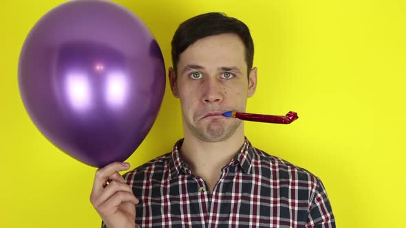 A Funny, Sad Guy with a Purple Balloon in His Hand Blows in a Party Horn Showing That He Is Not