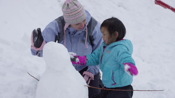 Mother and daughter building snowman together alt