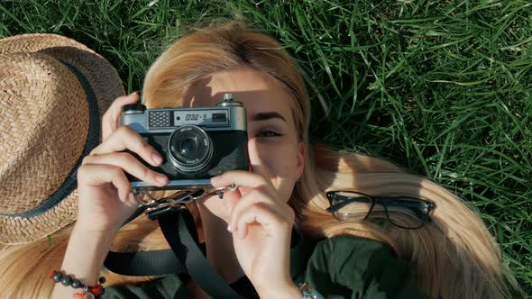 Young woman tourist lies on the grass and taking a picture on retro camera on vacation