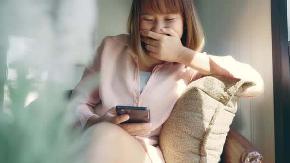Asian woman using smartphone for talking, reading and texting while sitting on table in cafe.