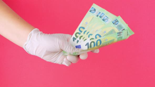 Hand in protective medical glove holds 100 EURO money bills pink color background Counting cash 4K