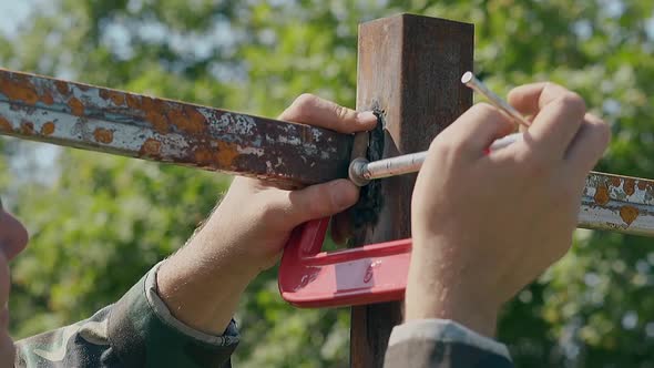Slow Motion Closeup Man Fixes Metal Plank with Clamp in Yard alt