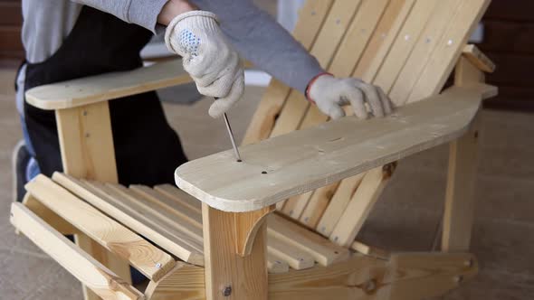 Young carpenter assembling wooden adirondack chair with screwdriver. alt