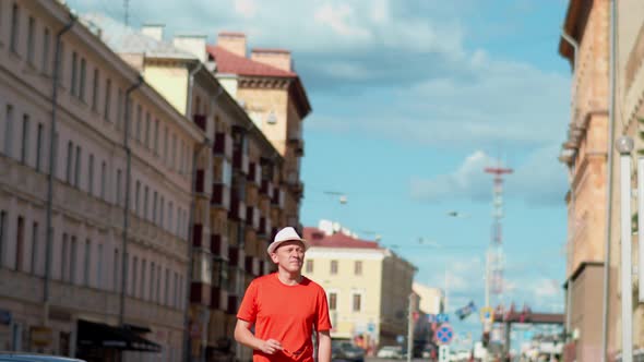 Young male tourist in hat walks along city street, camera tracking alt