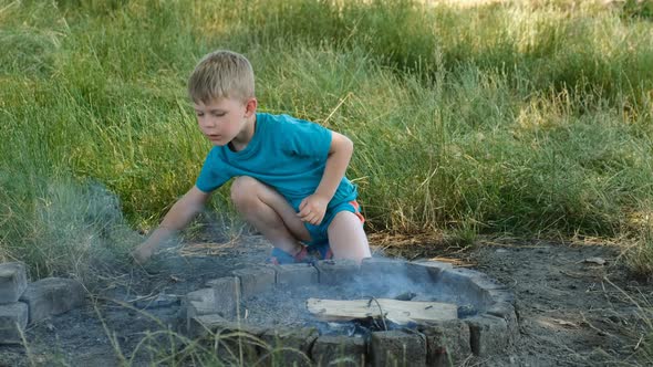 A small boy tries to light a fire with grass in nature in a special place.
