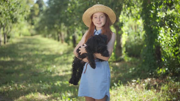 Happy Teenage Girl Posing with Black Norfolk Terrier in Summer Spring Park on Sunny Day alt
