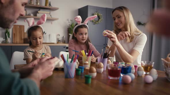 Zoom in of caucasian family of four people chatting and decorating easter eggs in domestic kitchen. alt