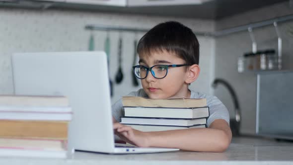 A Schoolboy Does Homework While Sitting in the Kitchen at the Table Using a Lot of Textbooks and a alt