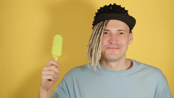 Young Handsome Man in Black Cap with Ice Cream on Yellow Background alt