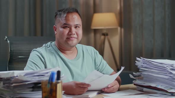 Close Up Of Fat Asian Man Smiling To Camera While Working With Documents At The Office alt