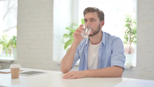 Young Creative Man Drinking Water in Modern Office alt